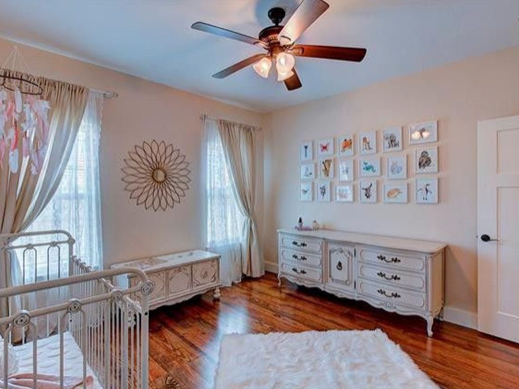 A full shot of the nursery room with droopers, a ceiling fan, decorative ornaments, a baby crib, and a wood musk floor.