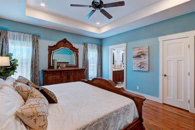 A full shot of a master bedroom with a wood musk floor, a master bed, a ceiling fan, and furnishings.
